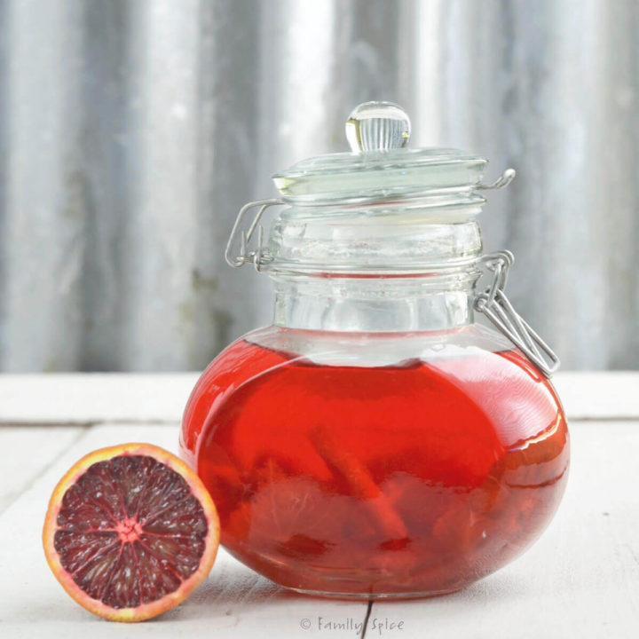 Blood oranges infusing vinegar in a glass jar with a blood orange next to it