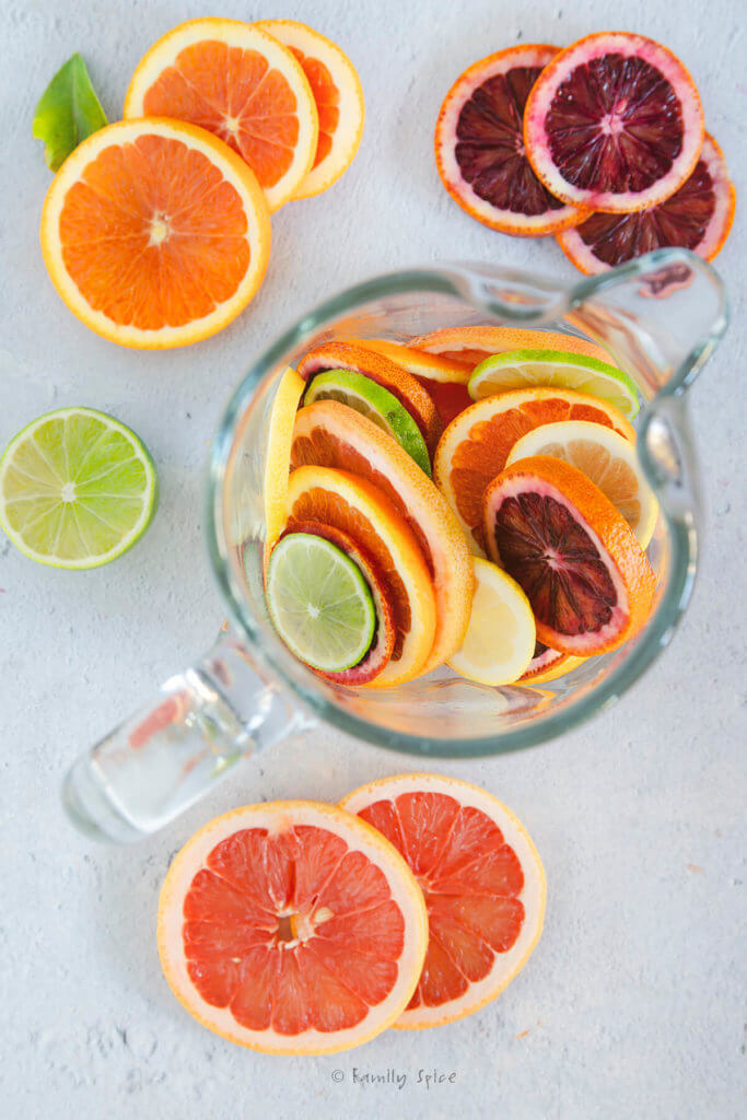 Various citrus slices in a clear pitcher with. more citrus clices around it