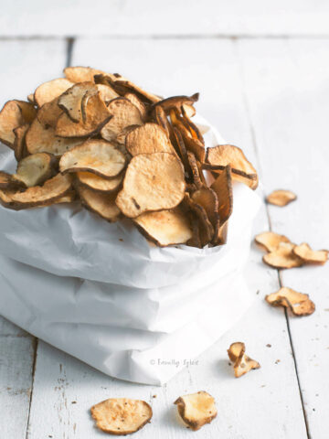 Side view of a white paper bag filled with baked jerusalem artichoke (sunchoke) chips