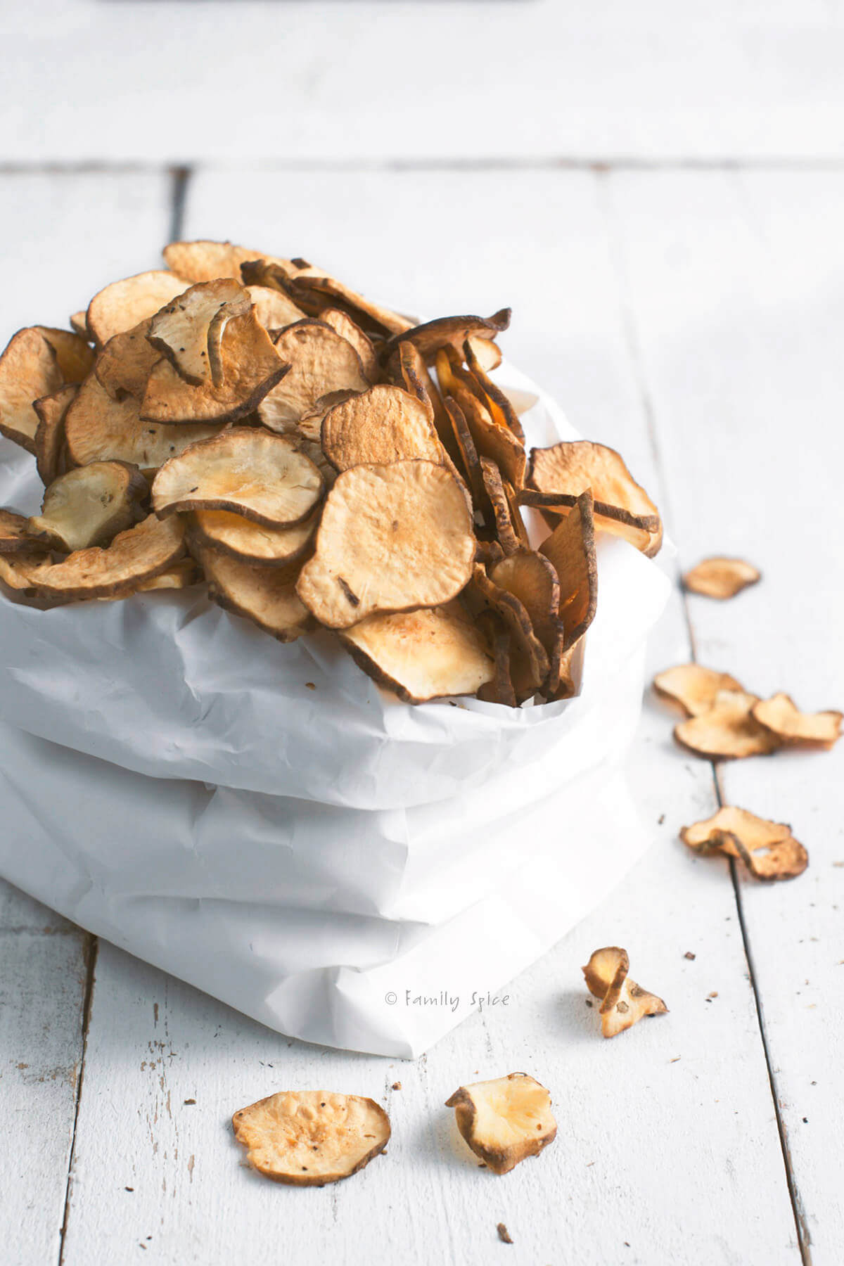 Side view of a white paper bag filled with baked jerusalem artichoke (sunchoke) chips