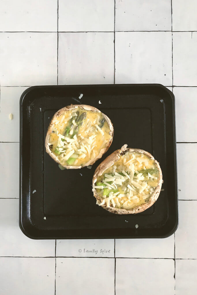 Top view of two portobello mushrooms with asparagus, cheese and egg mixture on a baking sheet