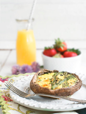 Side view of a portobello keto quiche in a cast iron pan with a carafe of orange juice and bowl of strawberries behind it