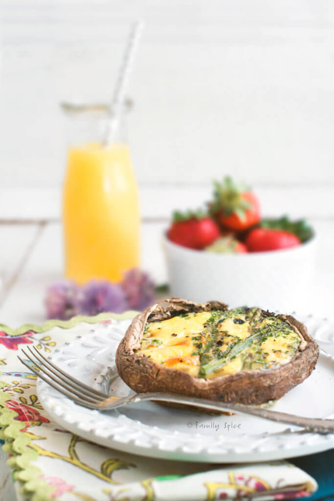 Side view of a portobello keto quiche in a cast iron pan with a carafe of orange juice and bowl of strawberries behind it