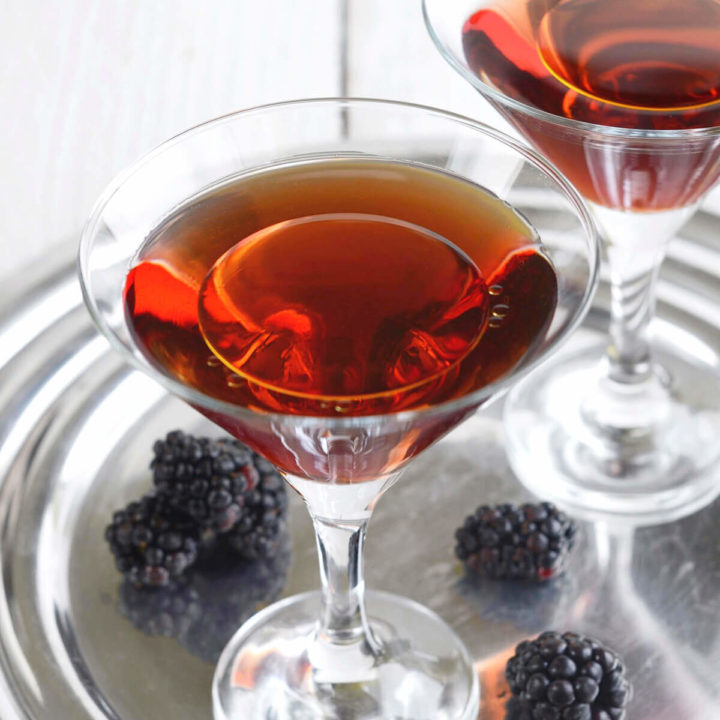 Closeup of two martini glasses with a blackberry cocktail in it and topped with a splash of olive oil