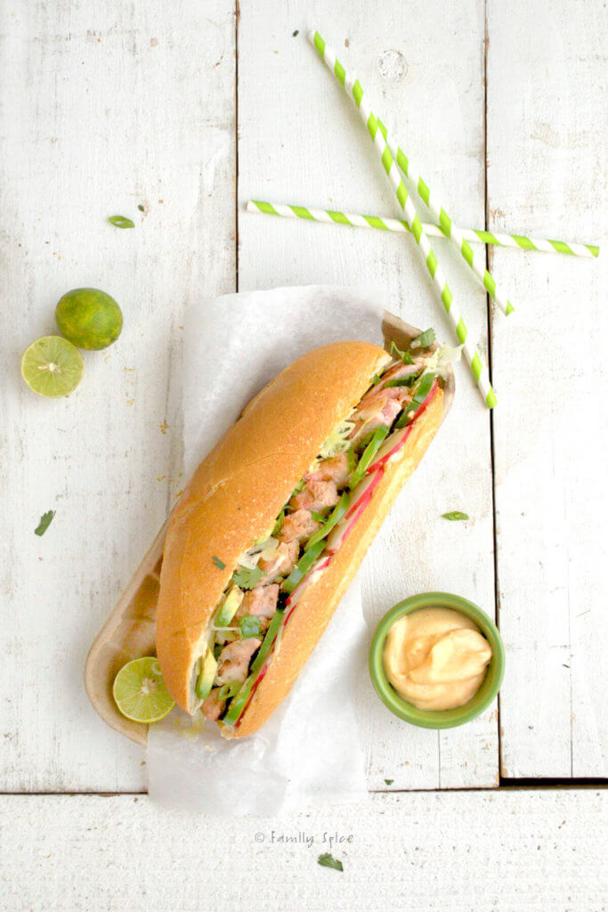 overhead view of a chicken banh mi sandwich stuffed with jalapeños, avocado, radishes, limes and sriracha mayonnaise
