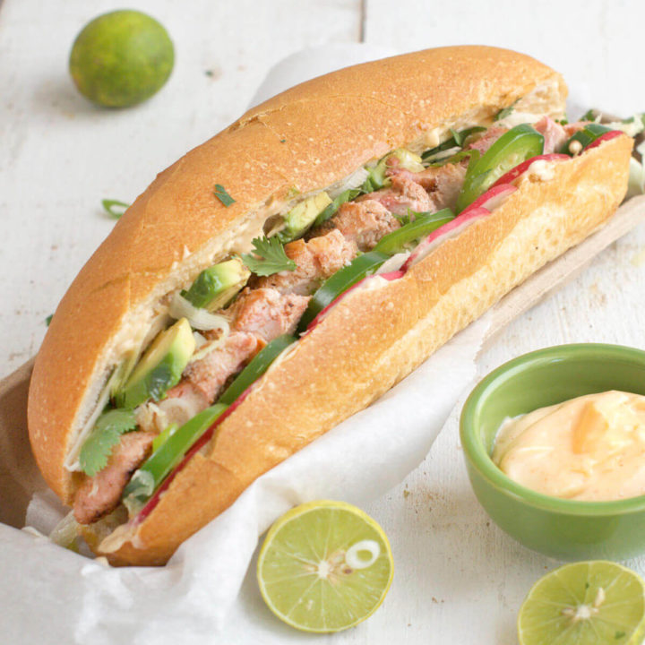 closeup of a chicken banh mi sandwich stuffed with jalapeños, avocado, radishes and sriracha mayonnaise