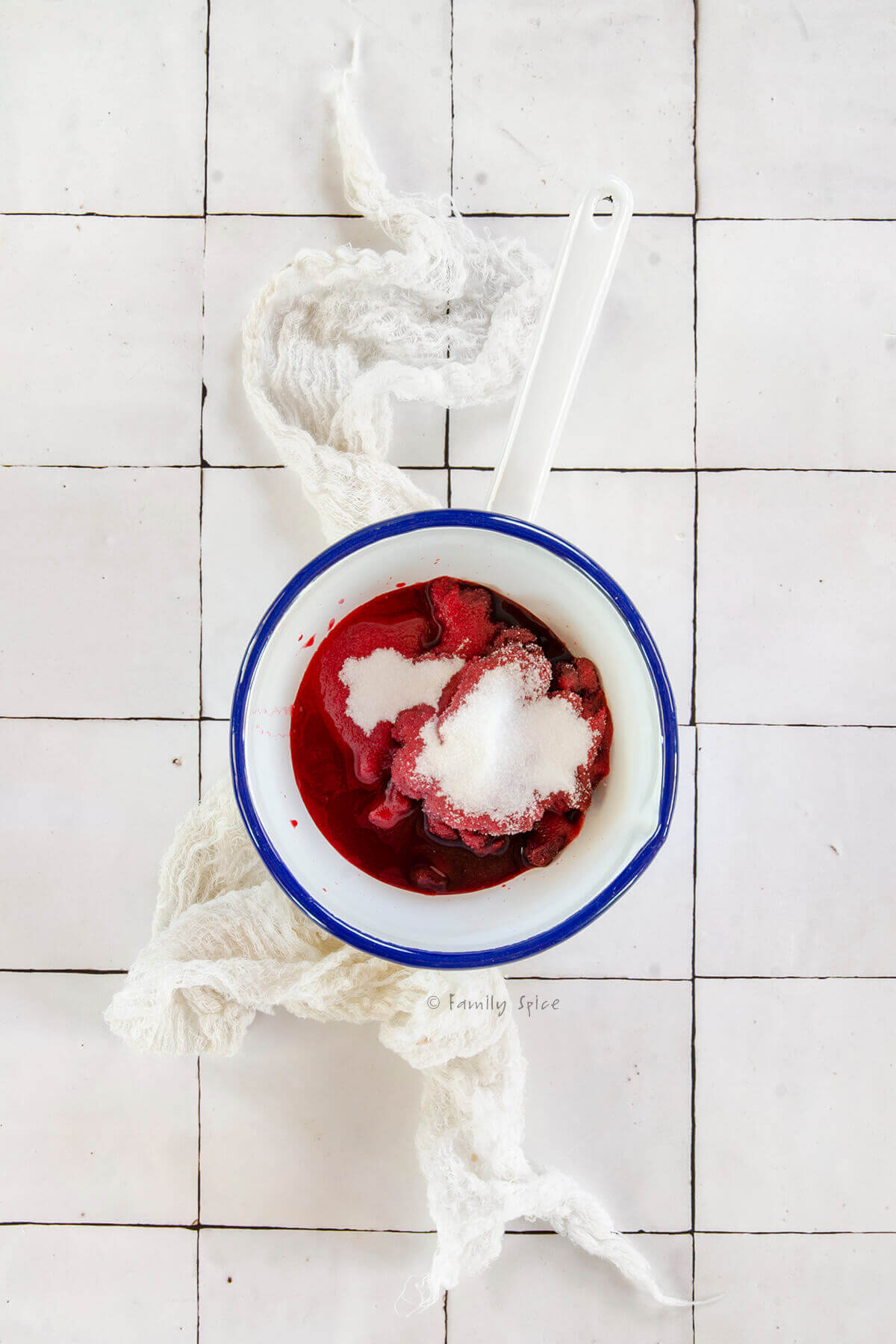 A white enamel pot with sour cherries and sugar in it