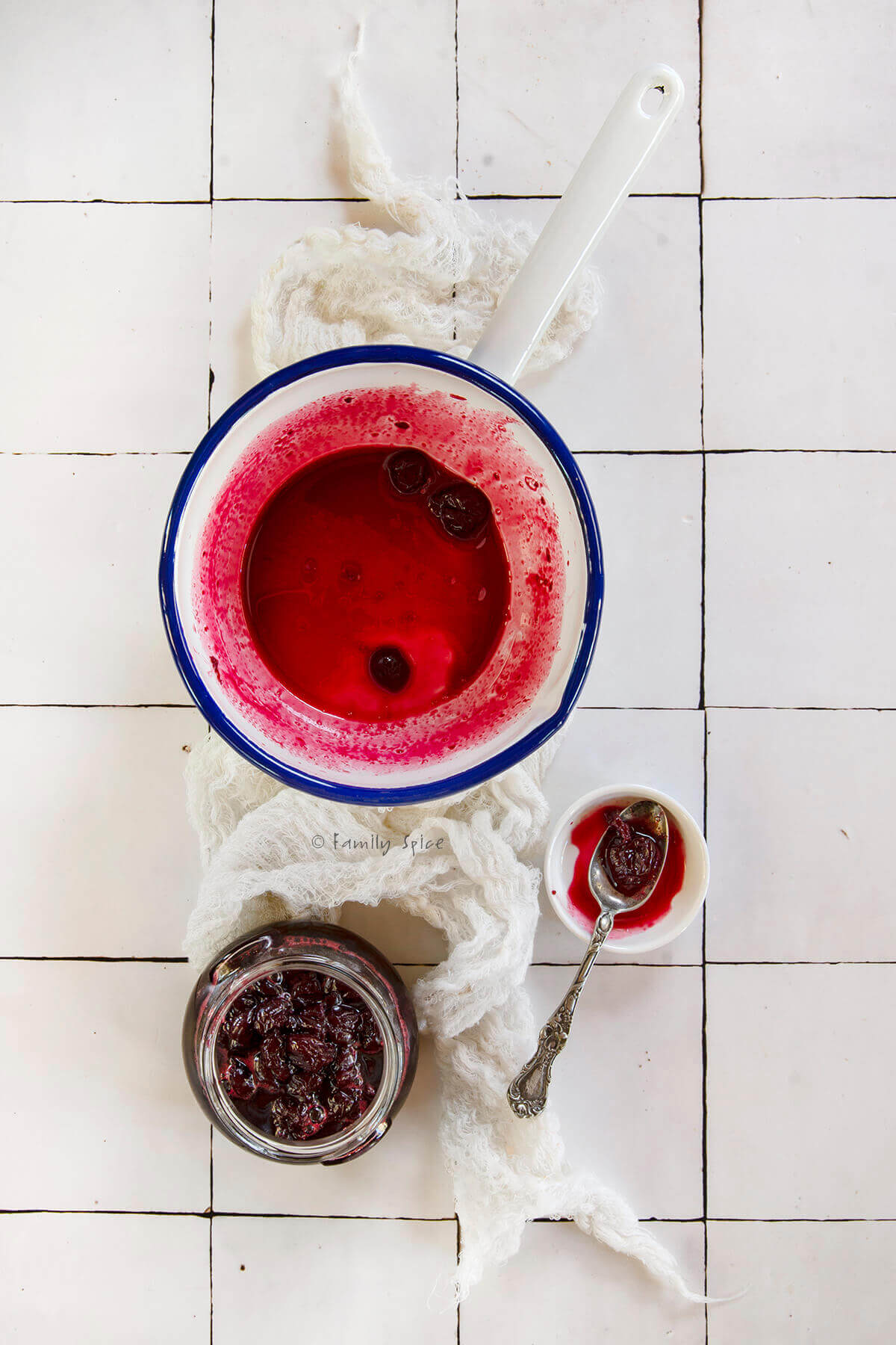 A white enamel pot stained with sour cherry jam juice and a jar of jam next to it