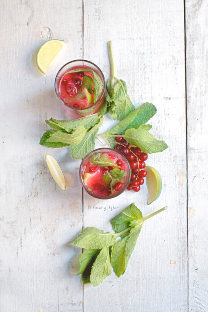 Top view of two glasses of red currant mojito with fresh mint, red currants and lime wedges next to it