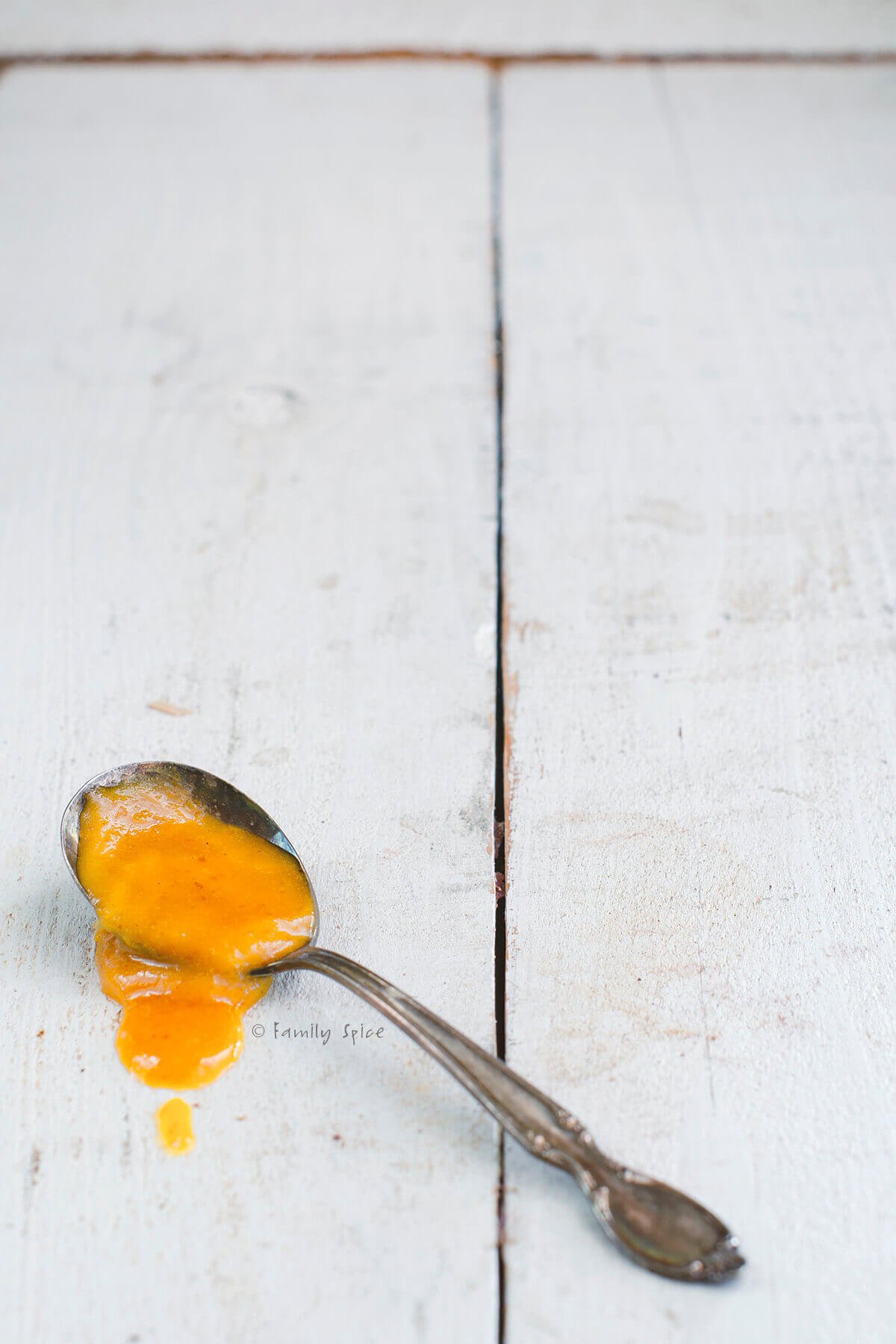 A spoon with pumpkin curd in it on a white wood table.