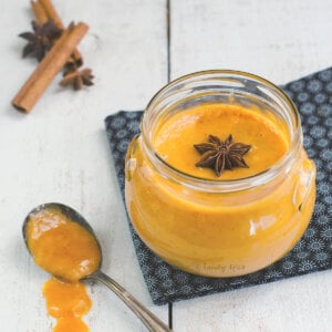 Closeup of a jar with pumpkin curd with a spoon, star of anise and cinnamon stick near it.