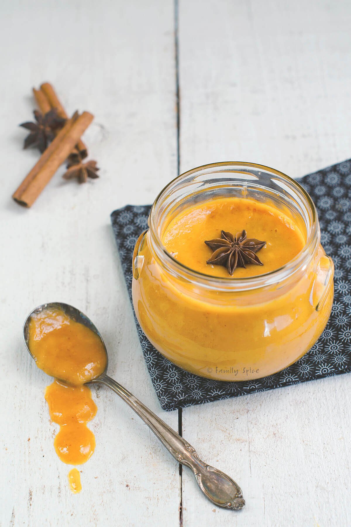 Closeup of a jar with pumpkin curd with a spoon, star of anise and cinnamon stick near it.