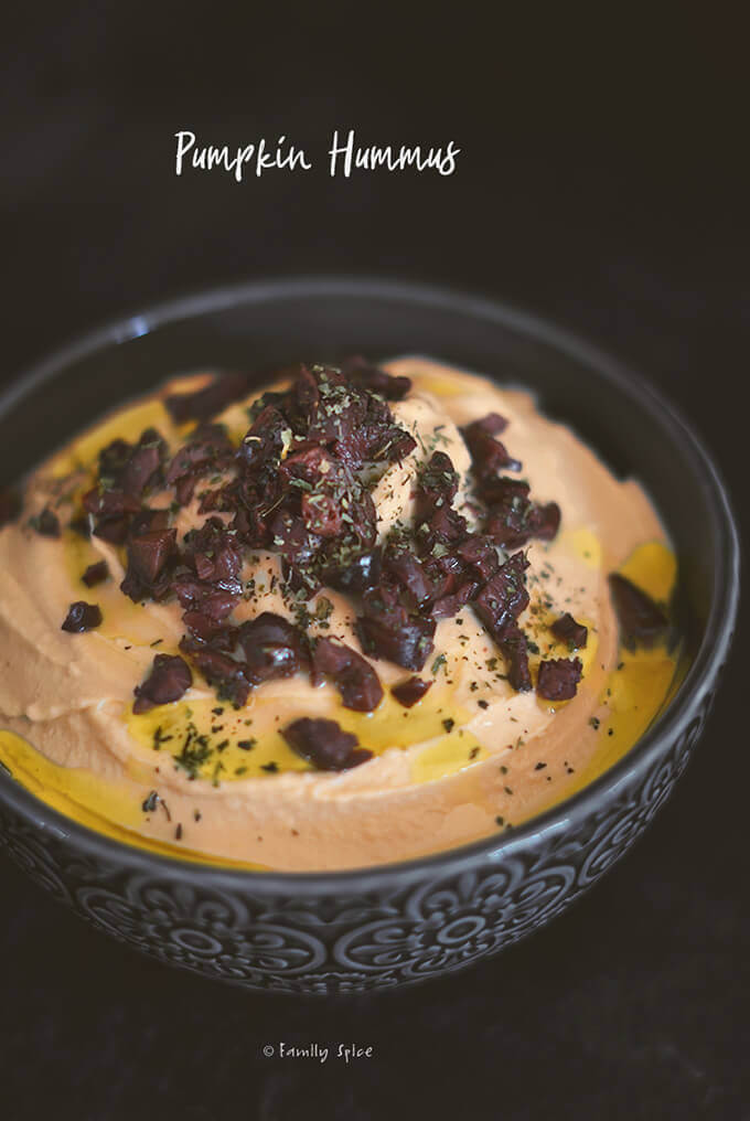 Closeup of a bowl full of pumpkin hummus garnished with black olives and olive oil by FamilySpice.com