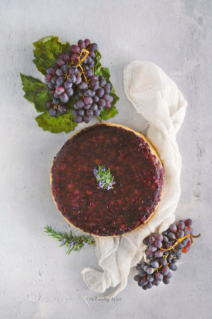 Top view of an upside down grape cake with fresh grapes and rosemary next to it