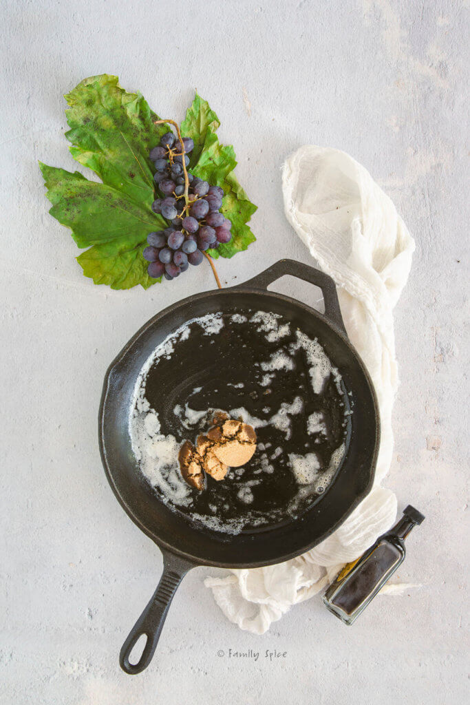 A cast iron skillet with melted and brown sugar in it and fresh grapes next to it
