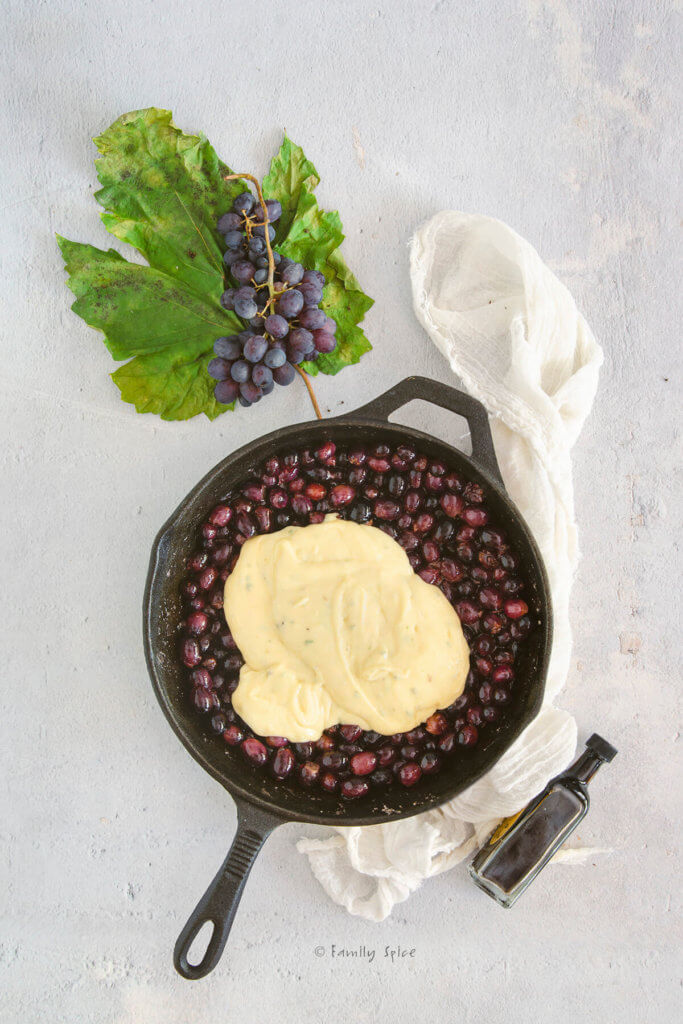 A cast iron skillet with cake batter over grapes in it and fresh grapes next to it
