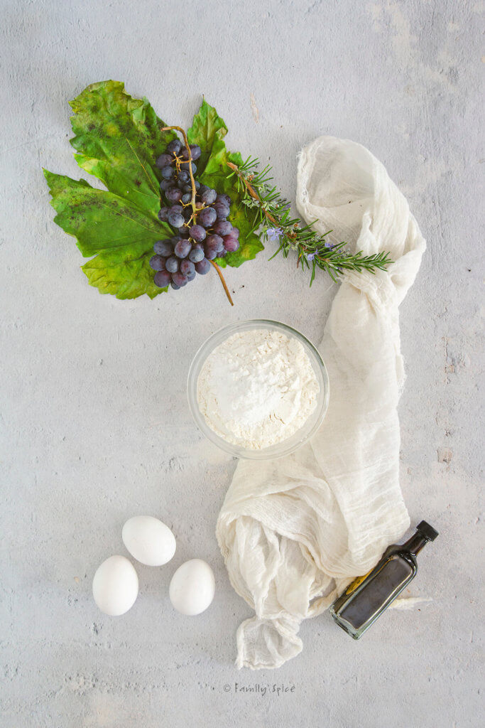 Flour mixture in a glass mixing bowl with eggs, a bunch of grapes and small bottle of balsamic vinegar next to it