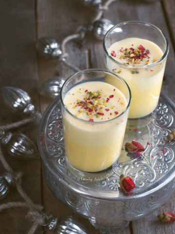 Two glasses of saffron eggnog garnished with rose petals and pistachios