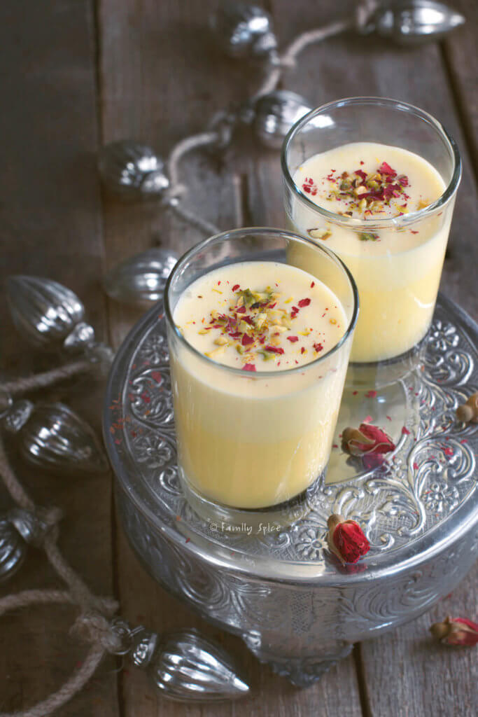 Two glasses of saffron eggnog garnished with rose petals and pistachios