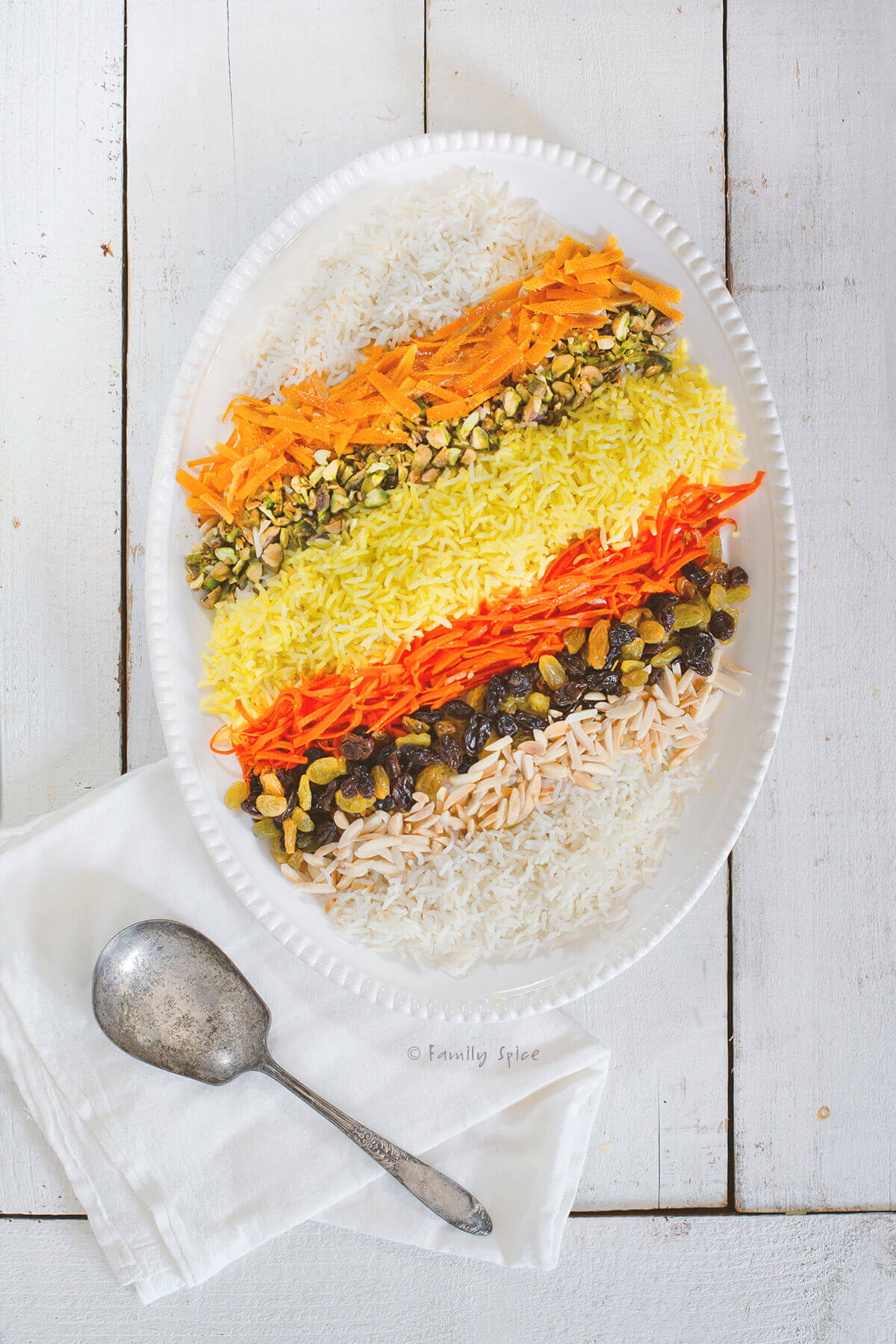 A platter of shirin polo (persian sweet rice) topped with candied orange slices, carrots, pistachios, almond slivers and saffron