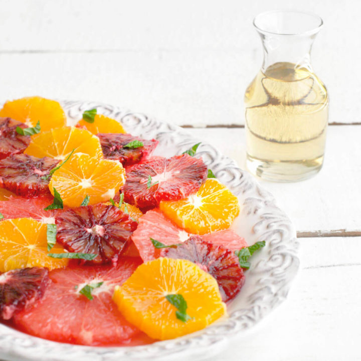 A citrus salad made with grapefruit, oranges and blood oranges on a platter with a small bottle of mint shrub
