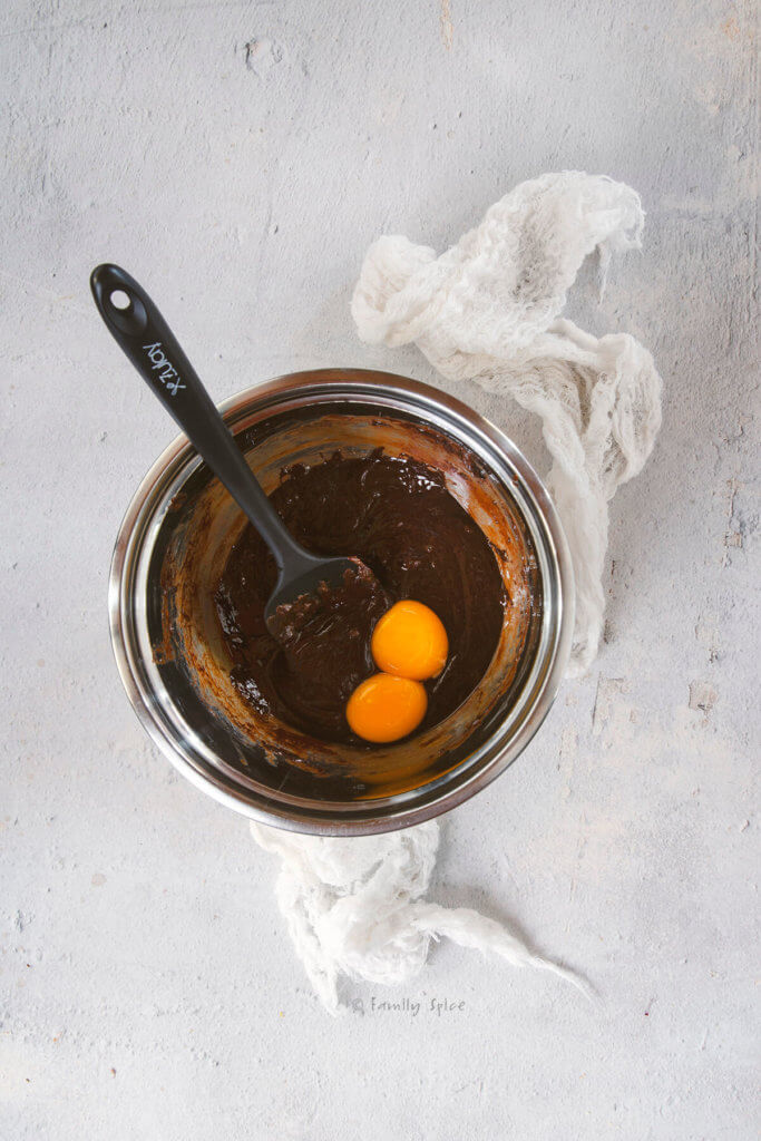 A stainless bowl with melted chocolate mixture and two egg yolks in it