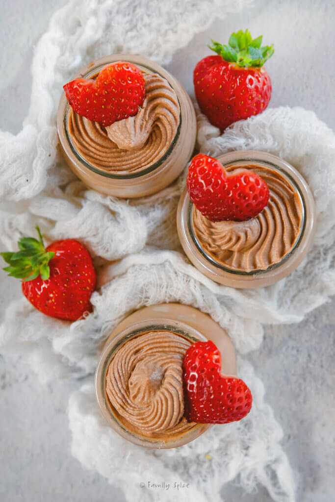 Dark chocolate mousse in small dessert jars with hearts cut from strawberries on top of it