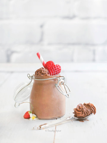 A closeup of a small mason jar filled with chocolate mousse and topped with a strawberry cut in the shape of a heart