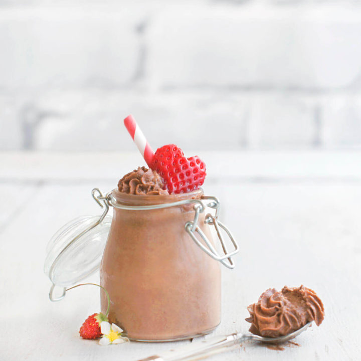 A closeup of a small mason jar filled with chocolate mousse and topped with a strawberry cut in the shape of a heart