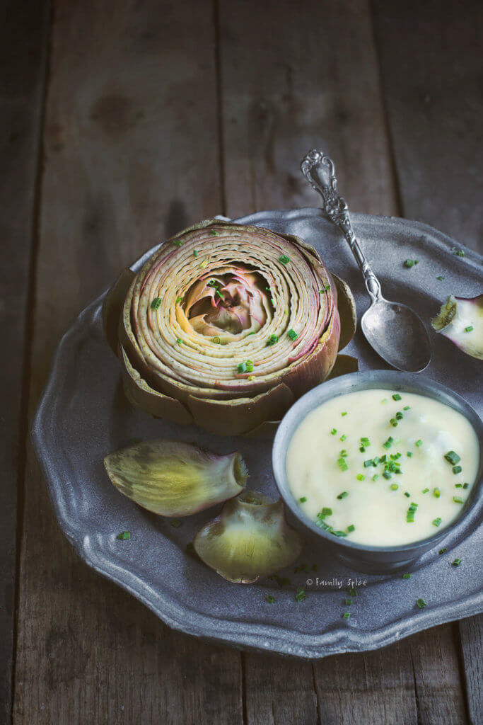 Close up of a pewter plate with a purple fiore viola steamed artichoke with a small bowl of garlic mayonnaise