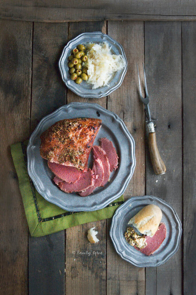 Top view of a corned beef roast with a slice on a plate with bread and a small plate with sauerkraut and olives next to it