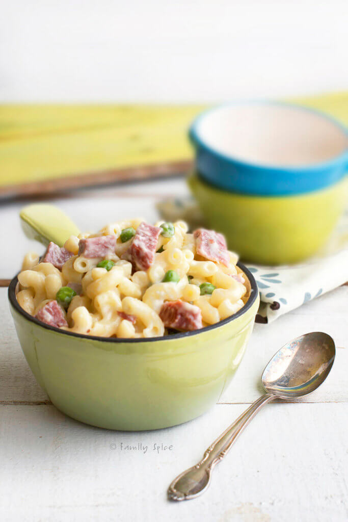 A small green pot with corned beef mac and cheese in it and small colorful bowls behind it