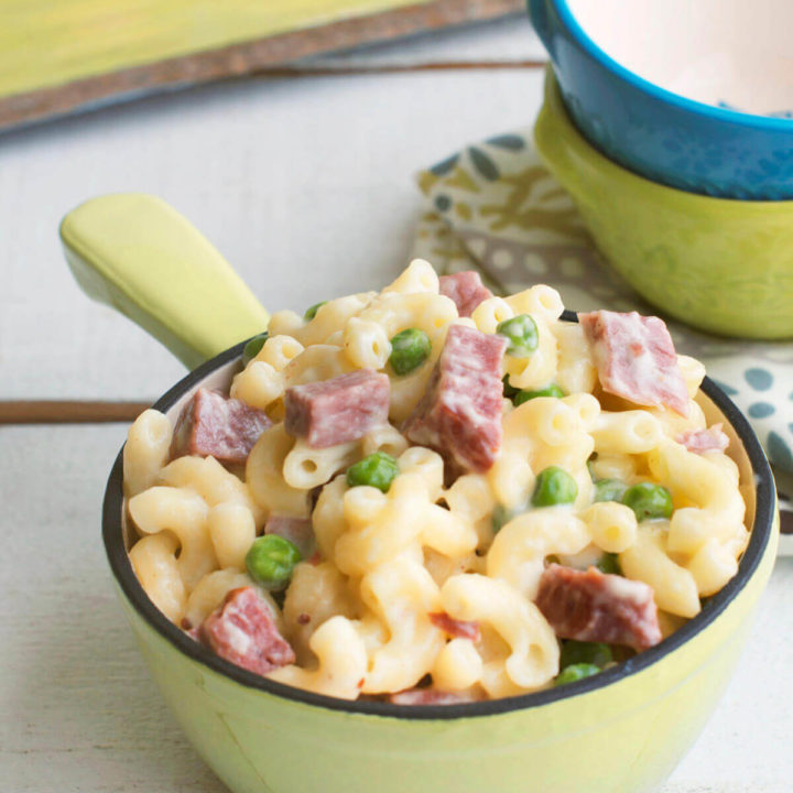 Closeup of a small green pot with corned beef mac and cheese in it and small colorful bowls behind it