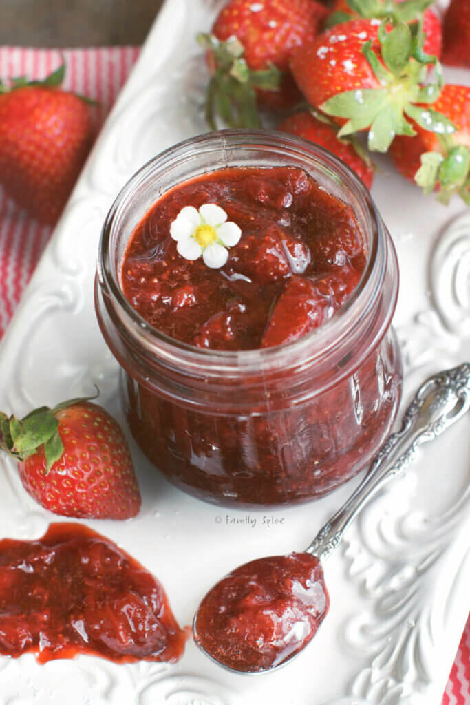 Top view of a small glass jar with strawberry jam in it and strawberries around it