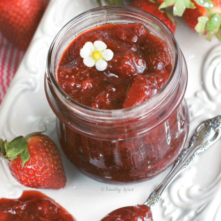 Top view of a small glass jar with strawberry jam in it and strawberries around it