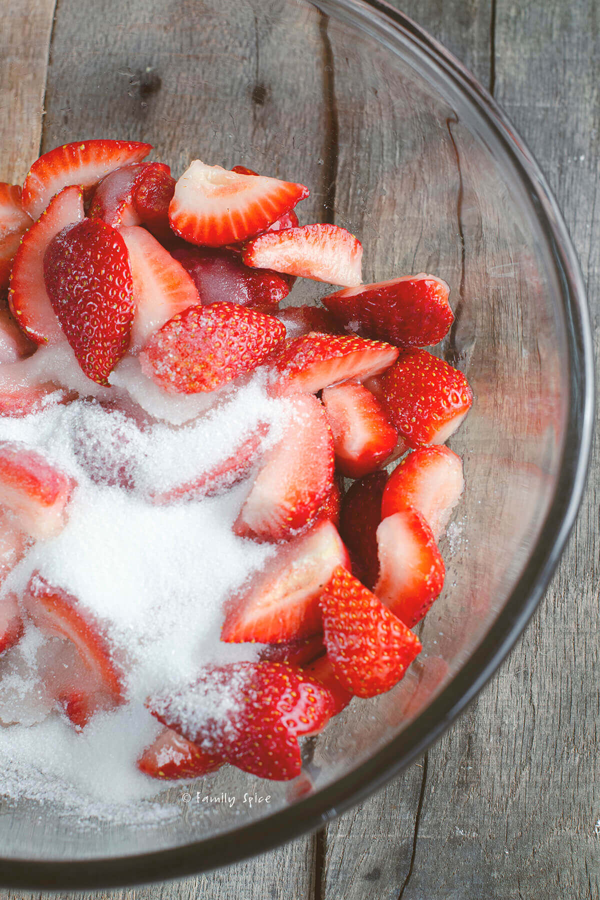 Closeup of chopped strawberries and sugar in a glass mixing bowl
