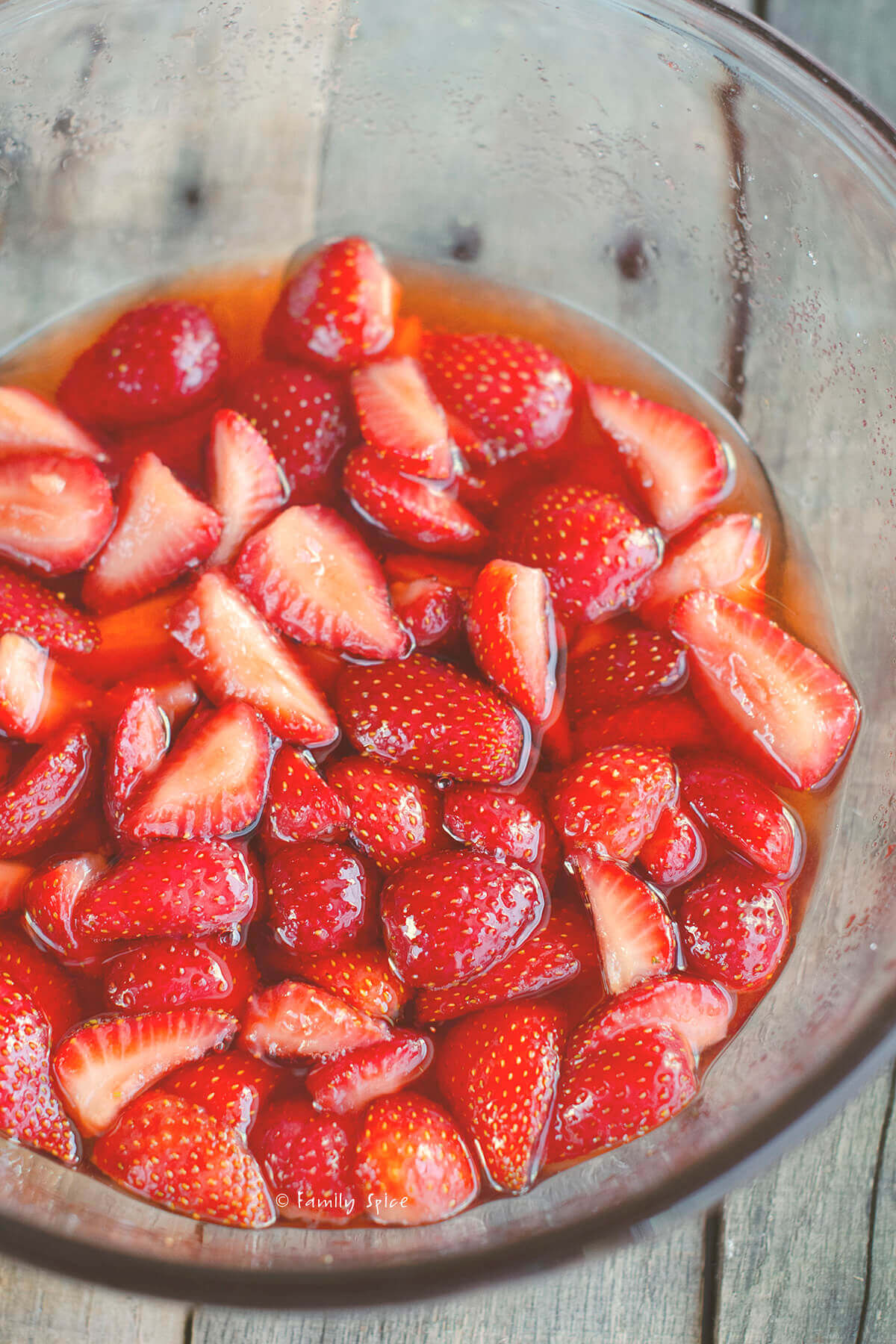 Closeup of chopped strawberries macerating in a glass mixing bowl