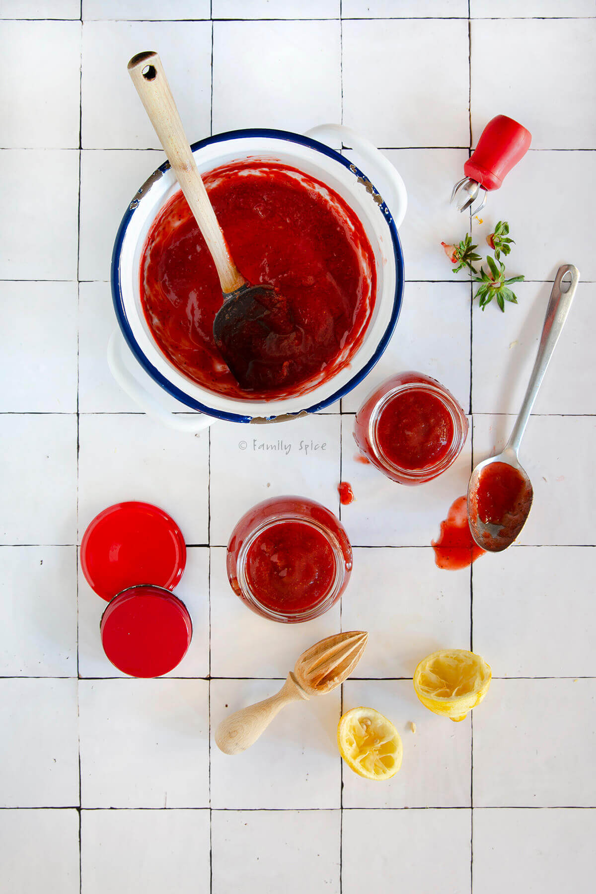 Top view of a pot of strawberry jam along with jars of jam and other kitchen items