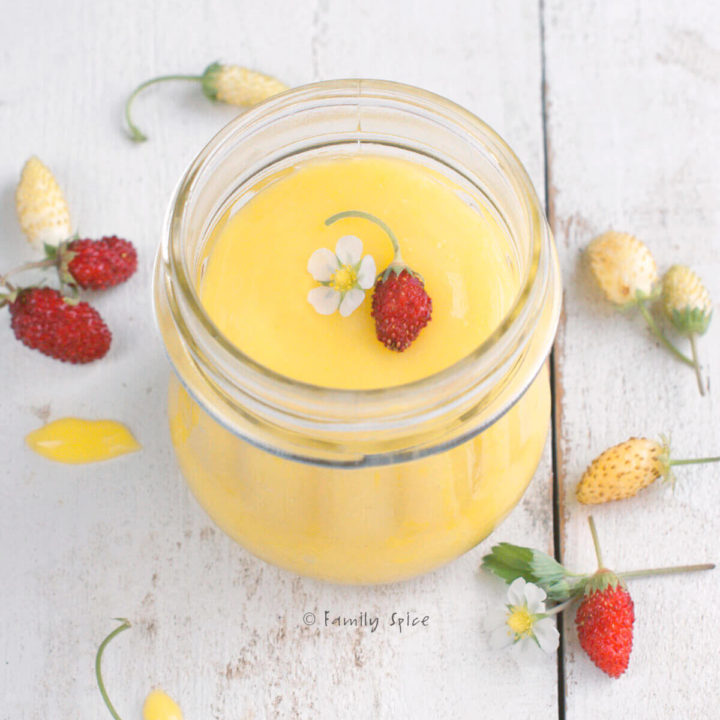 A small bottle filled with lemon curd with small strawberries around it