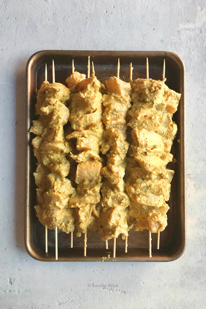 Marinated chunks of chicken breast on wooden skewers in a small baking sheet