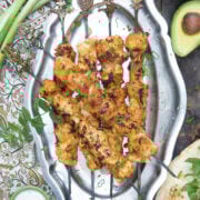 Closeup of top view of a metal platter with skewers of grilled chicken shawarma and vegetable sides around it
