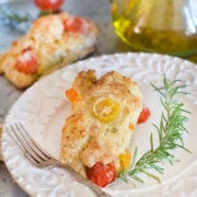 Closeup of a savory tomato scone on a white plate with a fork and sprig of rosemary with another scone behind it