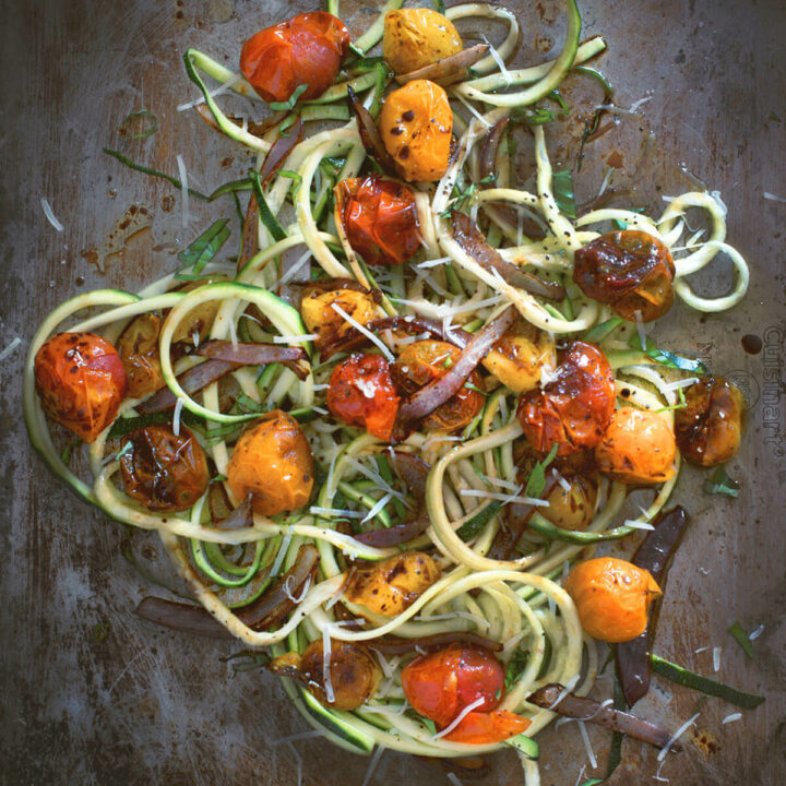 Top view of zucchini noodles (zoodles) and roasted tomatoes on a baking sheet