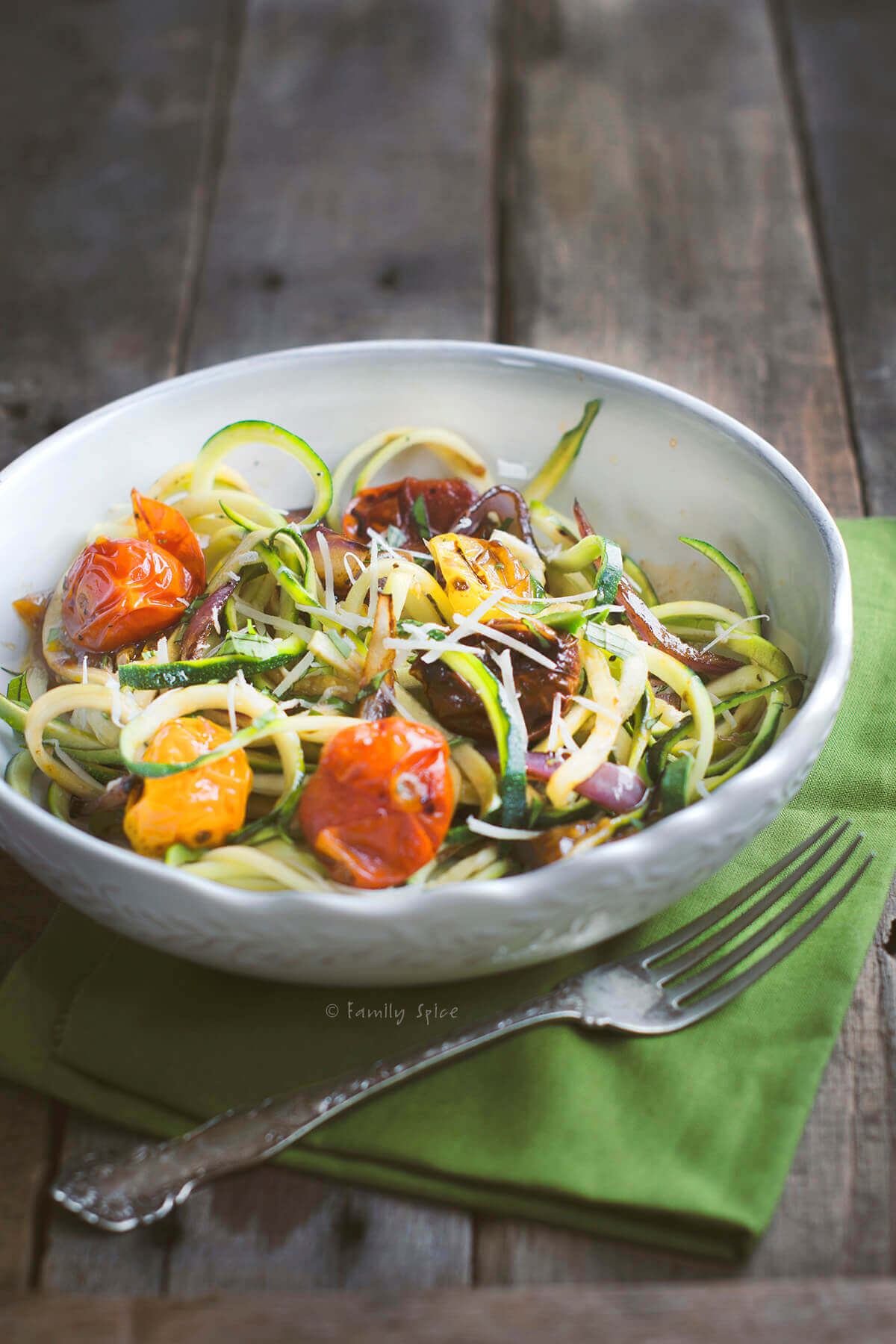 A white bowl with zucchini noodles (zoodles) and roasted tomatoes in it