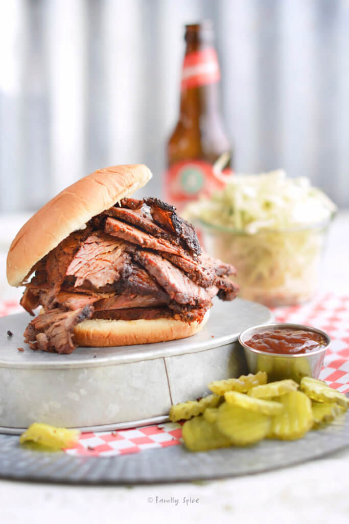 Side view of an overstuffed bbq brisket sandwich with pickles, coleslaw and beer