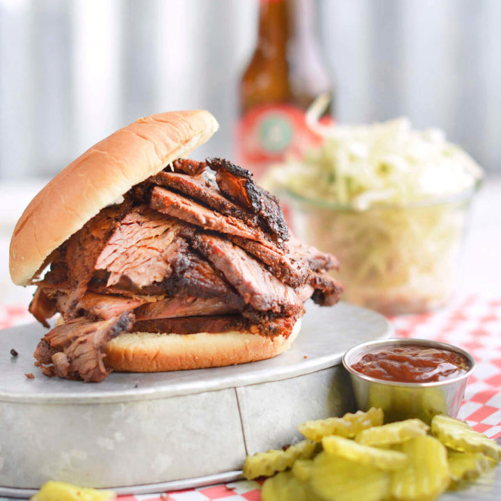 Side view of an overstuffed bbq brisket sandwich with pickles, coleslaw and beer