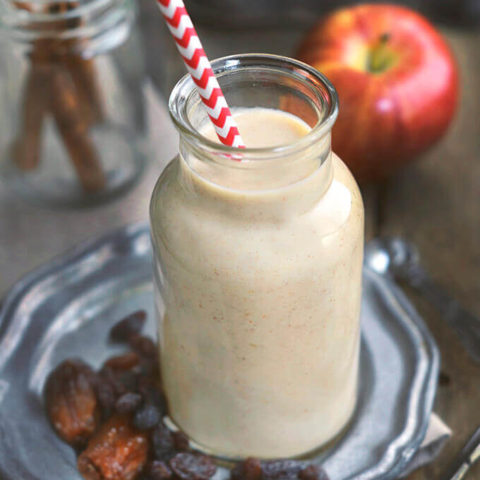 Close up of a small glass milk bottle filled with apple raisin smoothie surrounded by ingredients by FamilySpice.com