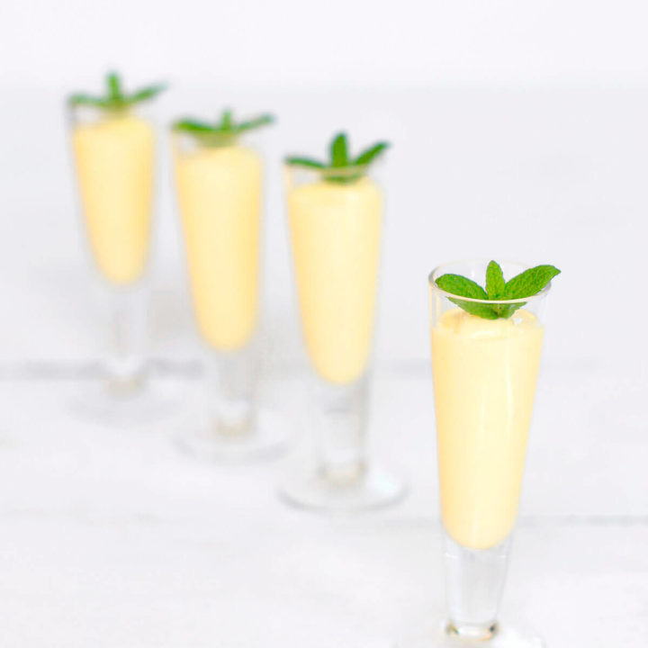 Four small shot glasses with mango rum smoothie in them and topped with fresh mint