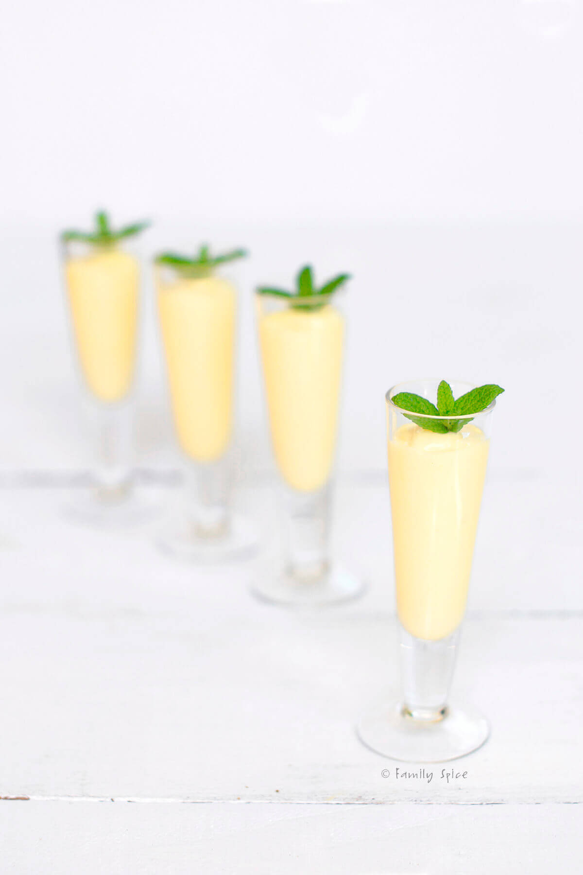 Four small shot glasses with mango rum smoothie in them and topped with fresh mint
