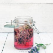 A small mason jar with sage blossom infused vinegar in it and sage blossom next to it